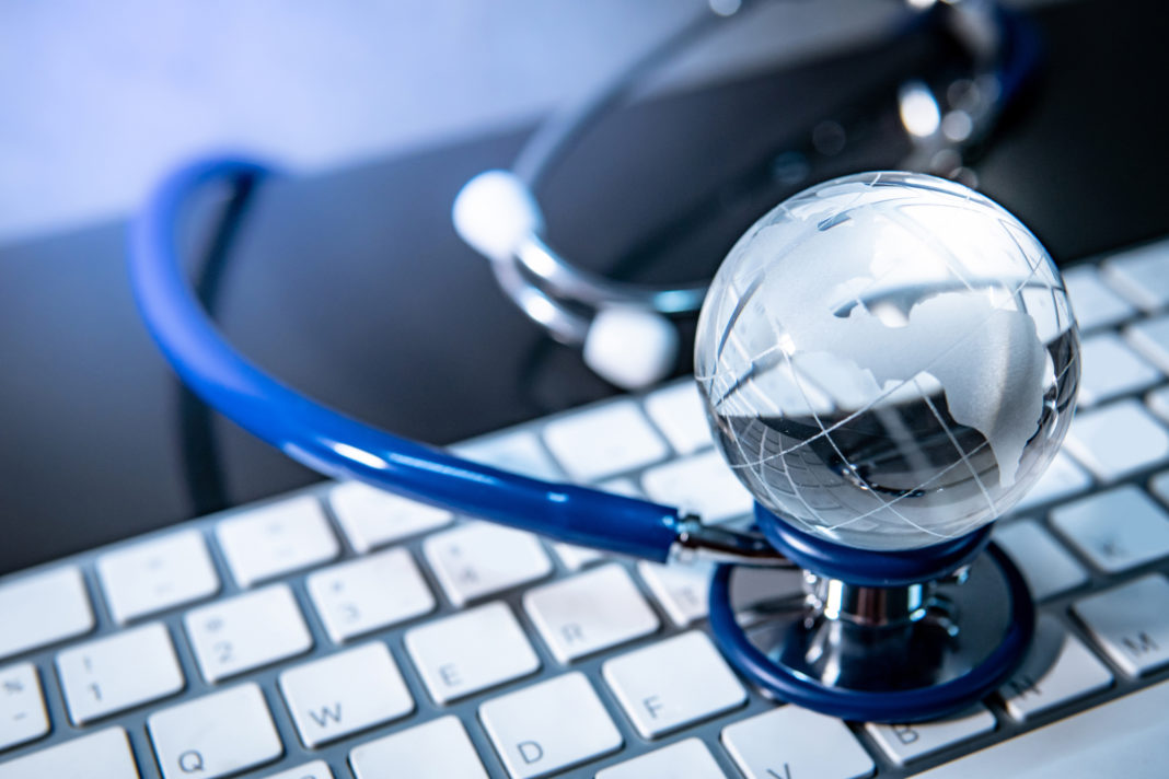 Global healthcare concept. World globe crystal glass on blue stethoscope on white keyboard. Health and medical science. Worldwide wellness business and technology