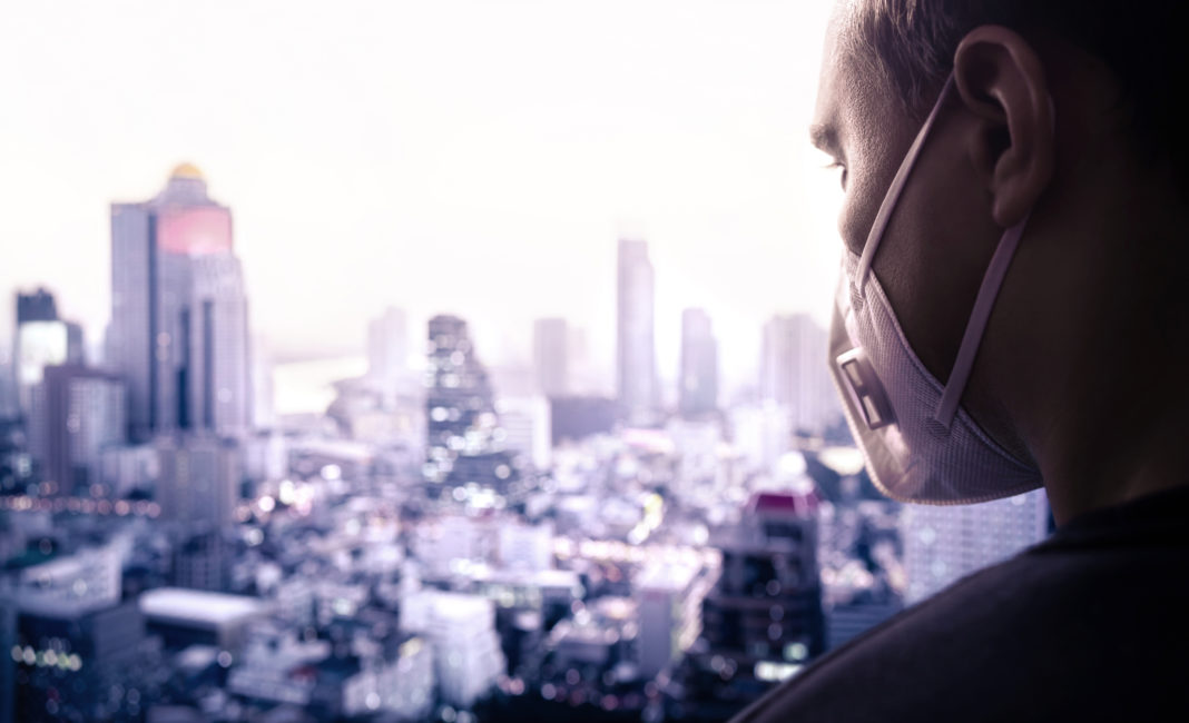 Pollution or virus mask in city. Protecting from polluted contaminated air or influenza or coronavirus. Man wearing facemask on rooftop. Disease, infection or smog protection.
