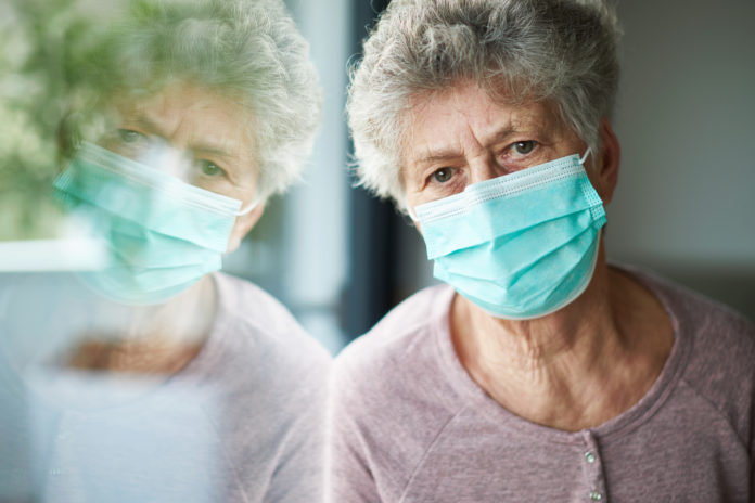 a old woman or grandma is wearing a respirator or surgical mask and looking out of the window