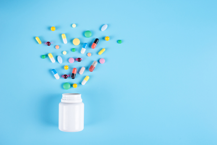 Assorted pharmaceutical medicine pills, tablets and white bottle on blue background. Copy space for text