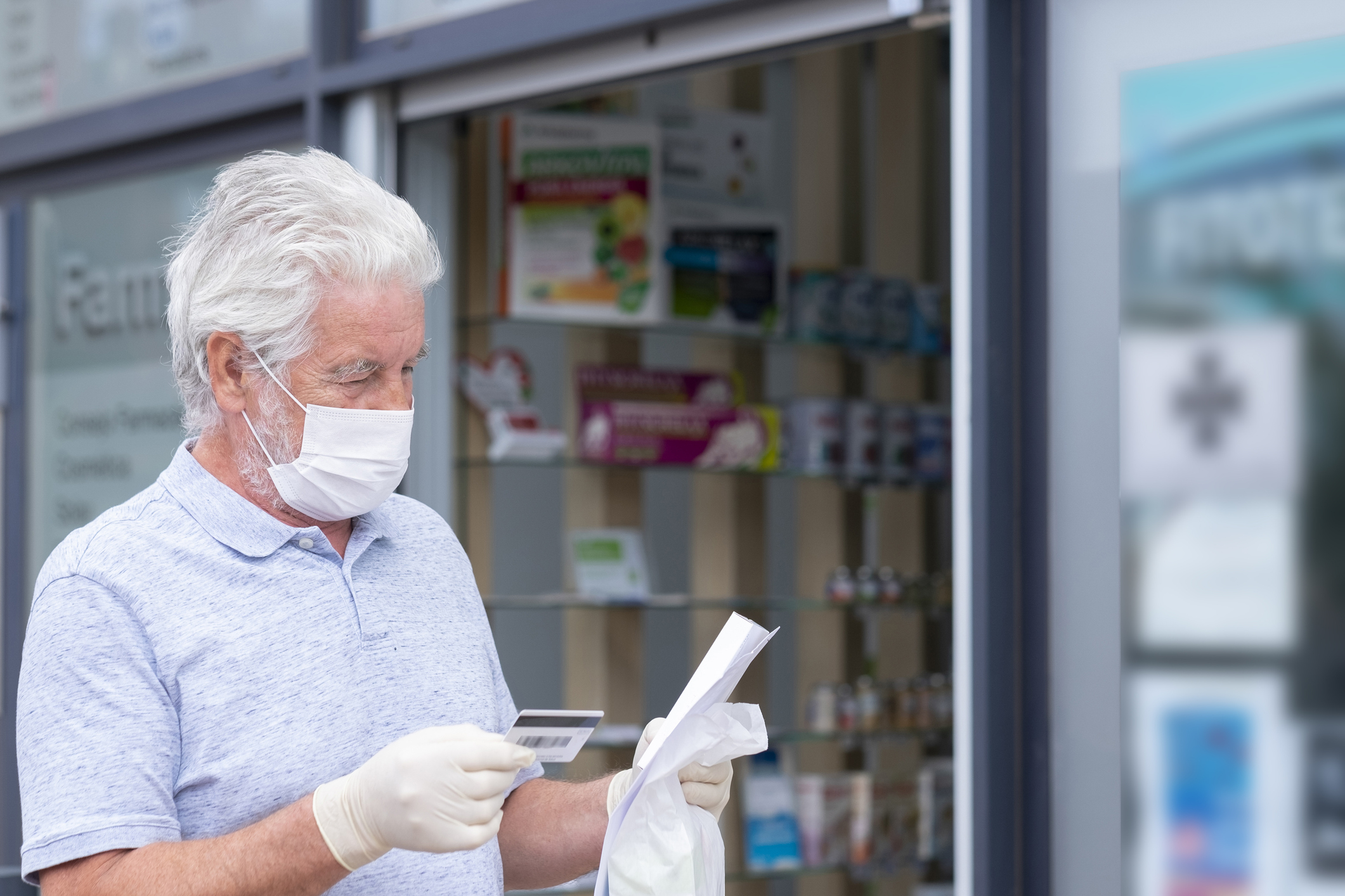Elderly man with mask and protective gloves leaves the chemist's shop with medicines and instructions. Fear of coronavirus infection, covid-19. Concept of retired senior and fear of contagion vacunación