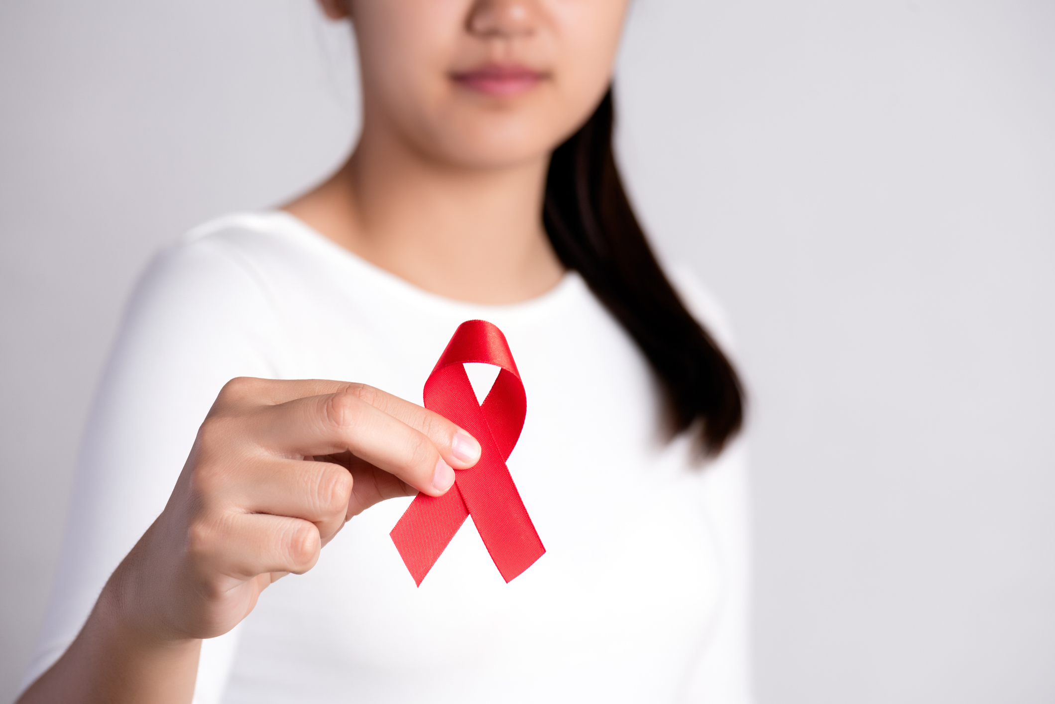 Closeup woman hand holding red ribbon HIV, world AIDS day awareness ribbon. Healthcare and medicine concept.